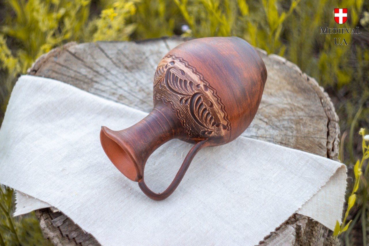 Hand-carved red clay pitcher lying on its side, revealing botanical leaf pattern on the shoulder