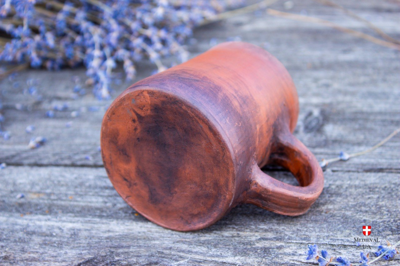 Handmade red clay medieval cup tilted to show its smooth base and earthy milk-fired tones