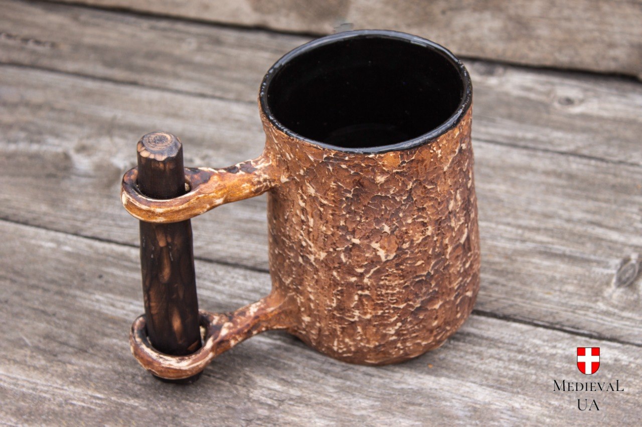 Ceramic medieval tavern tankard on weathered wood, with a rough milk-fired surface and hand-sculpted crossbar handle