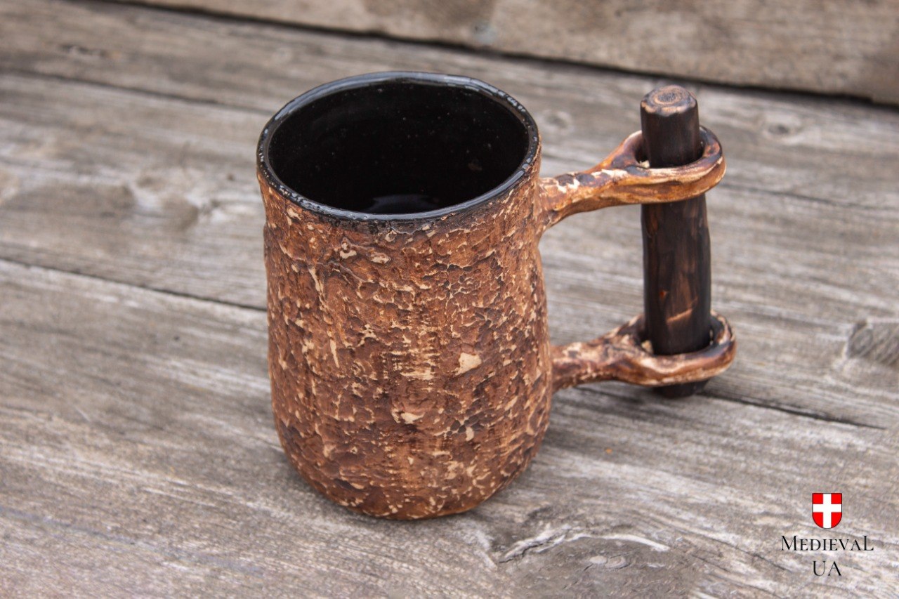 Handmade ceramic beer mug on grey wooden boards, showing the black glazed interior and textured milk-fired body