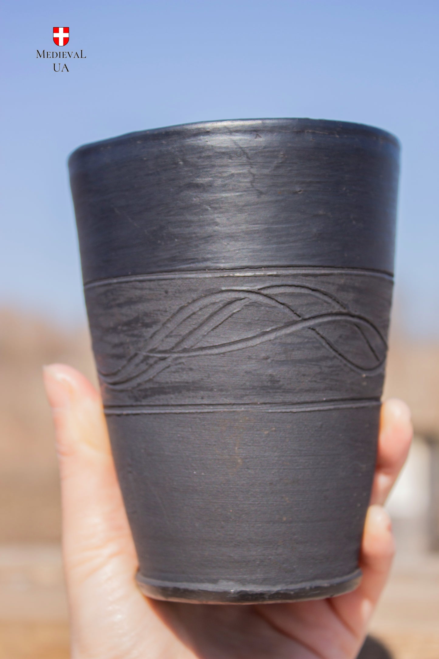 Hand holding a matte black medieval clay chalice