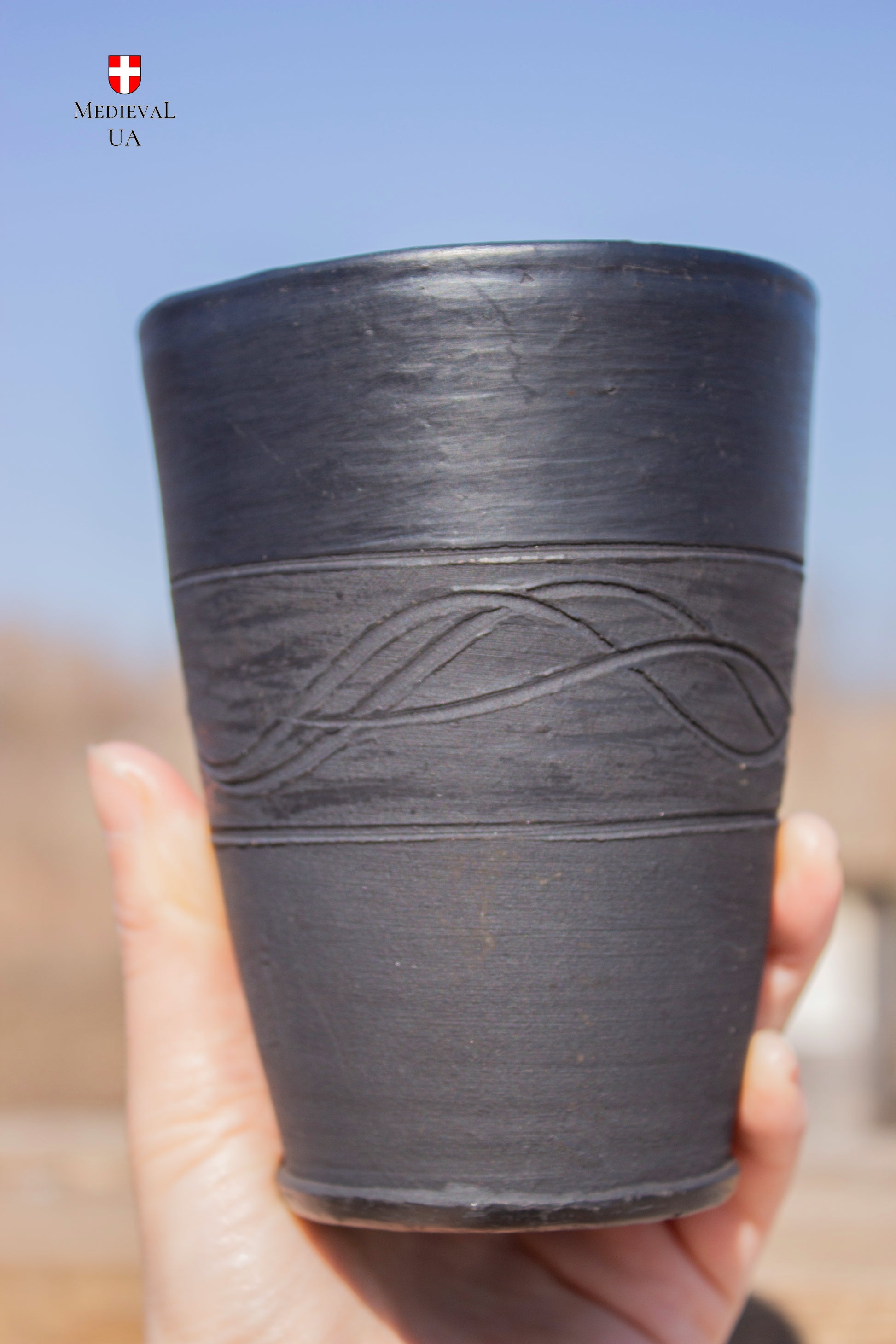 Hand holding a matte black medieval clay chalice