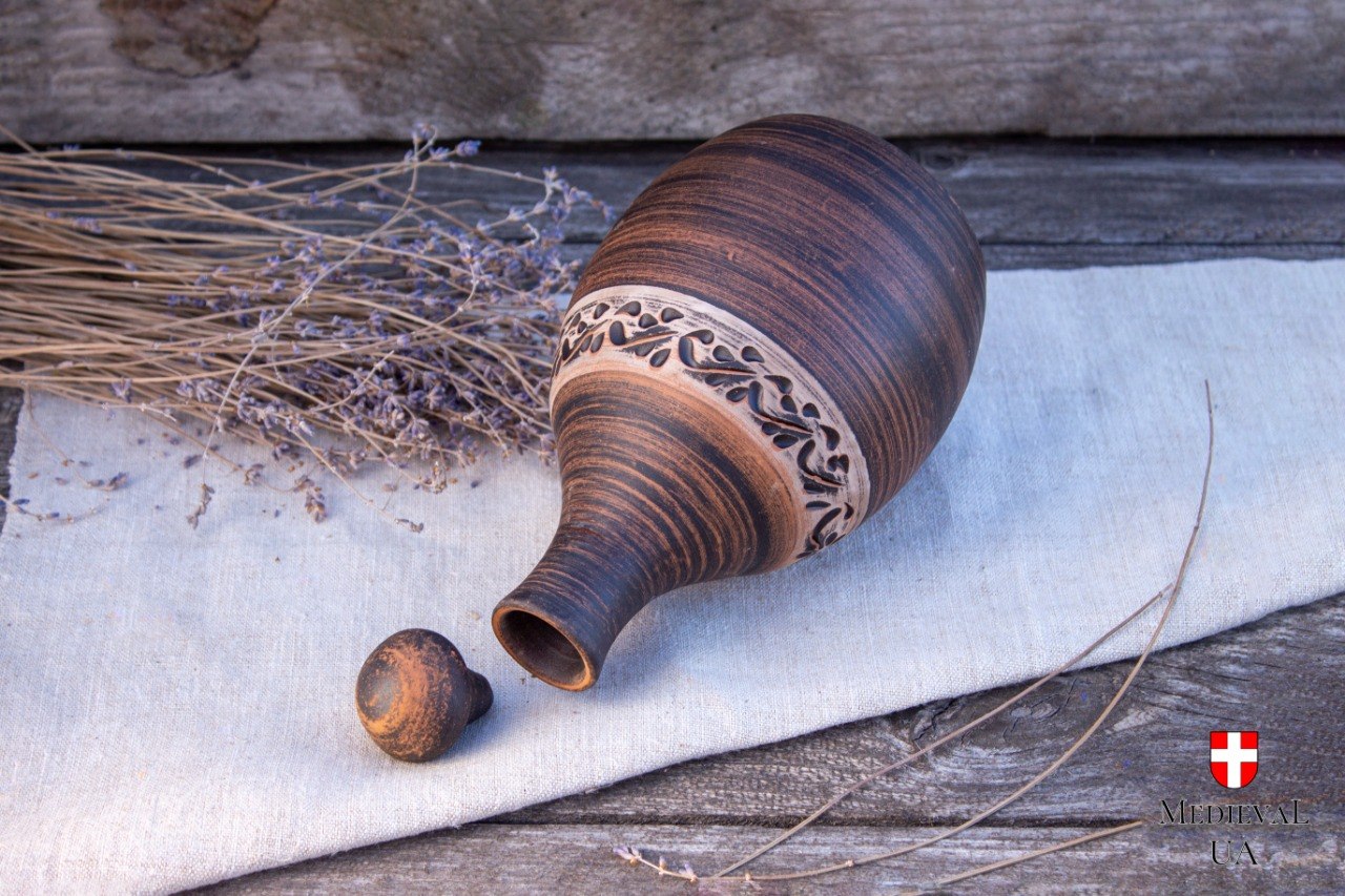 Carved red clay mead bottle on its side beside its ceramic stopper