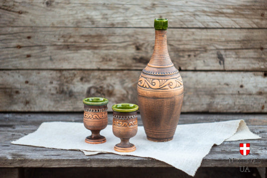 Complete Celtic mead set with clay bottle and two green-glazed goblets on linen and rustic wood