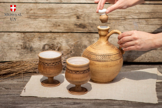 Hand holding a handmade ceramic wine goblet with a carved triangle pattern in a sunny green meadow