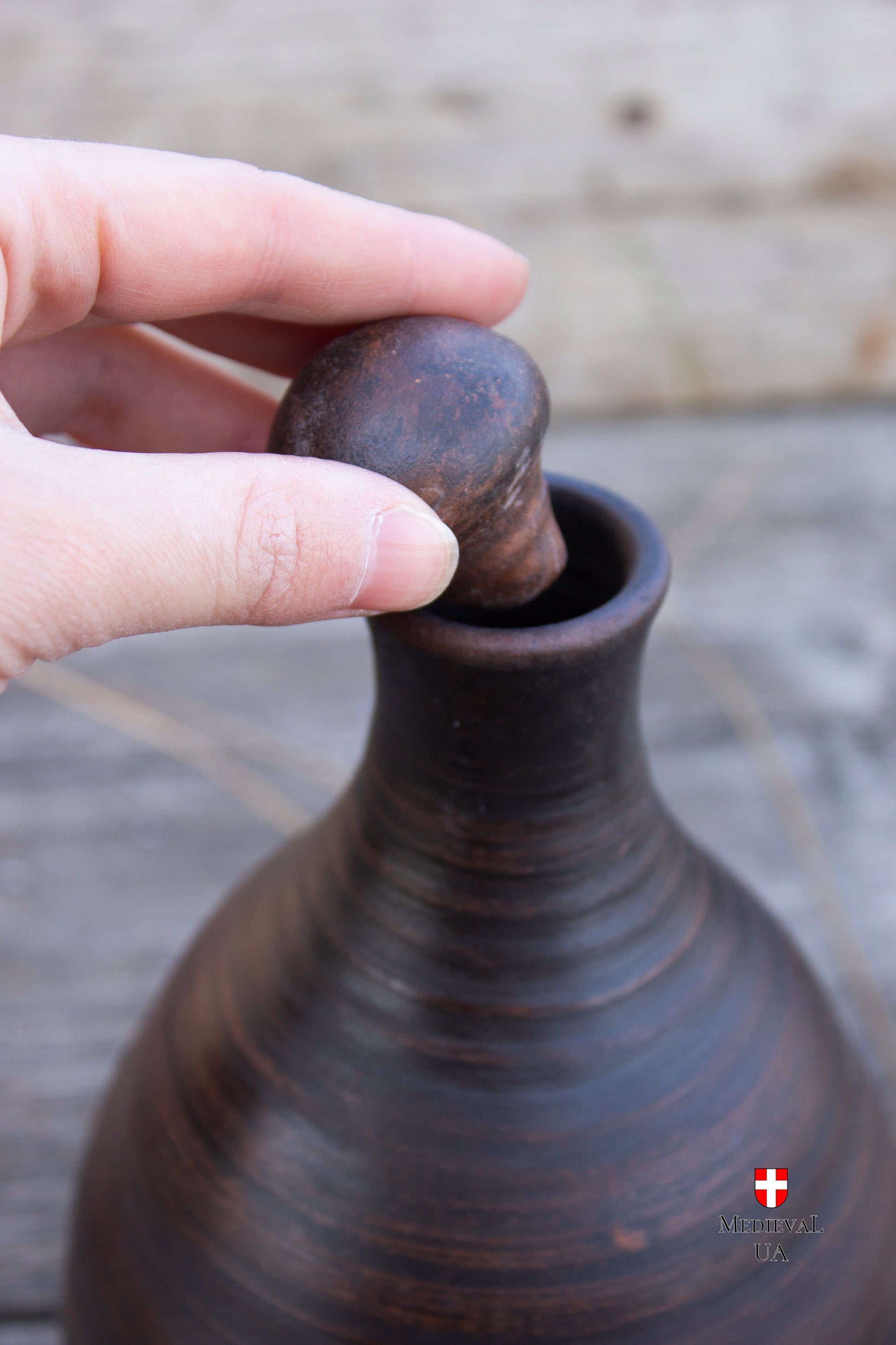 Round ceramic stopper being set into the neck of a clay bottle