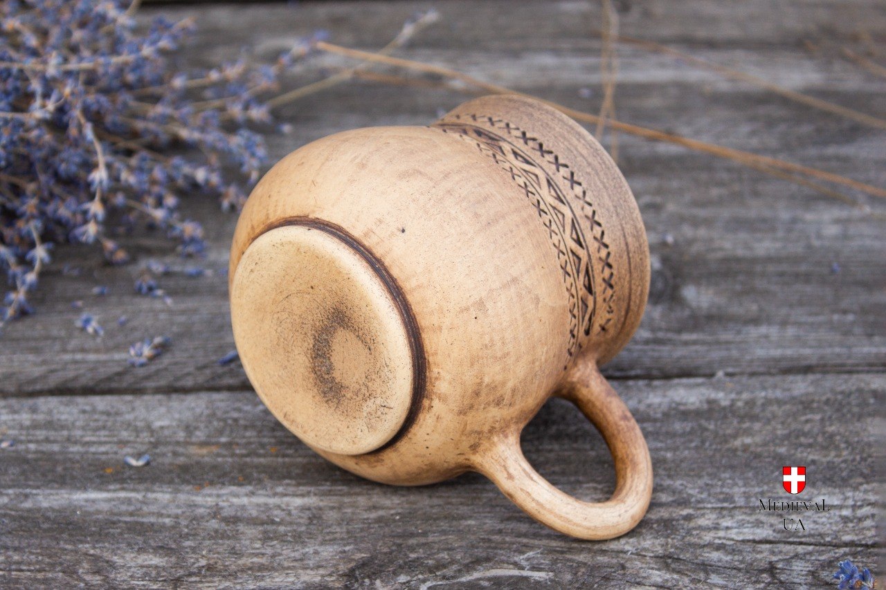 Base view of the handmade engraved clay mug showing the footed bottom and folk pattern