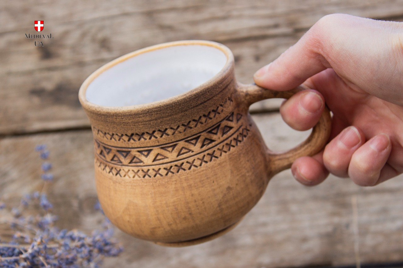 Engraved rustic clay mug held in hand, showing the white food-safe glazed interior