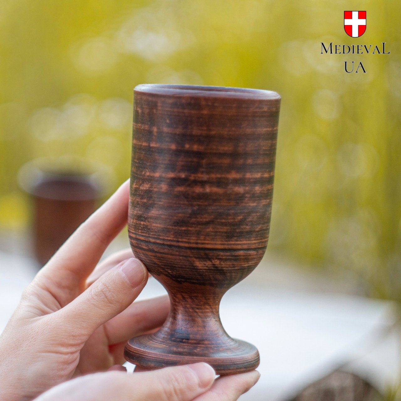 Single footed red clay goblet held up, revealing rippled terracotta surface from milk firing