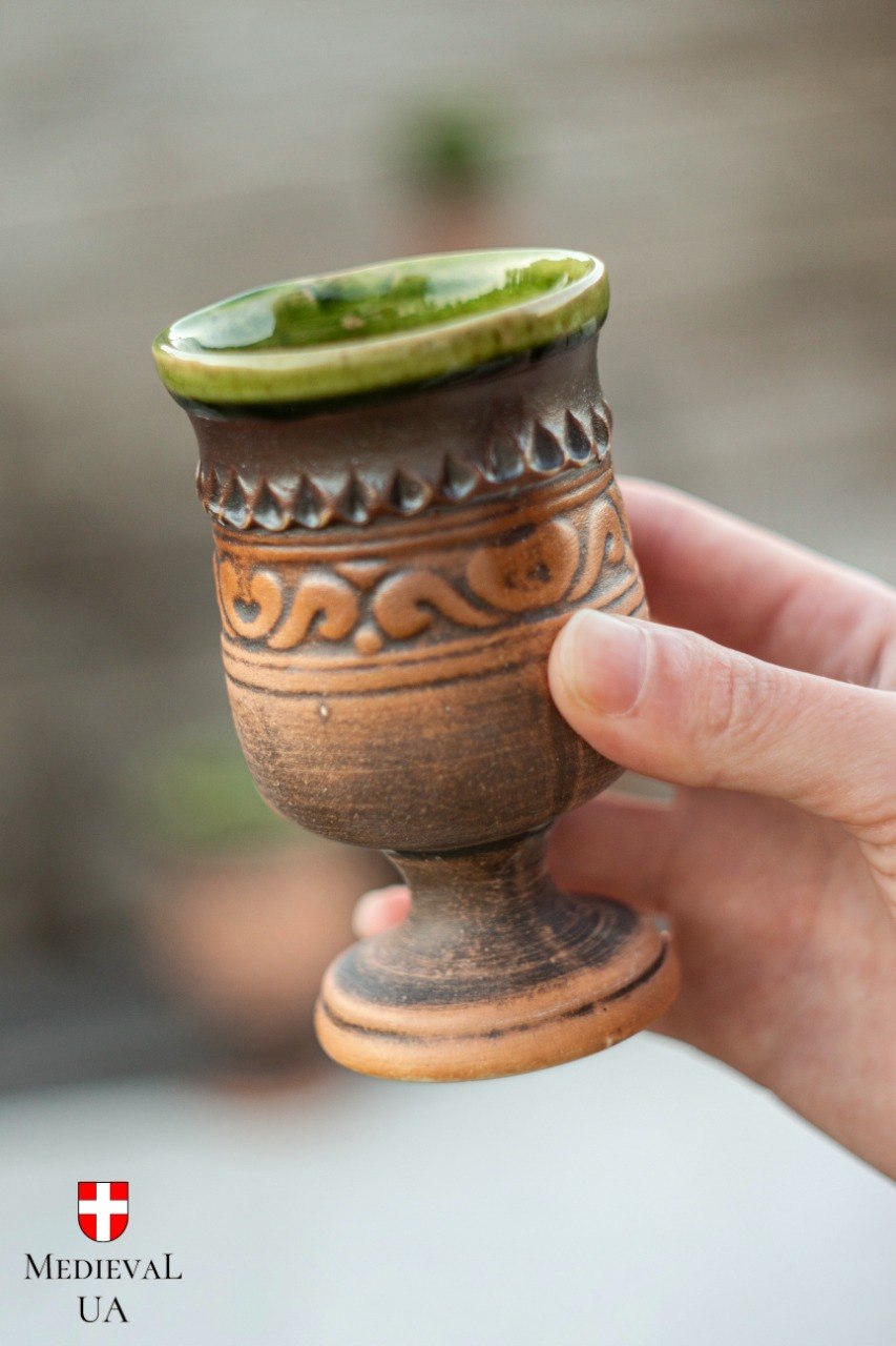Handmade ceramic mead goblet held in hand, brown clay body with carved folk relief and glossy green glaze rim