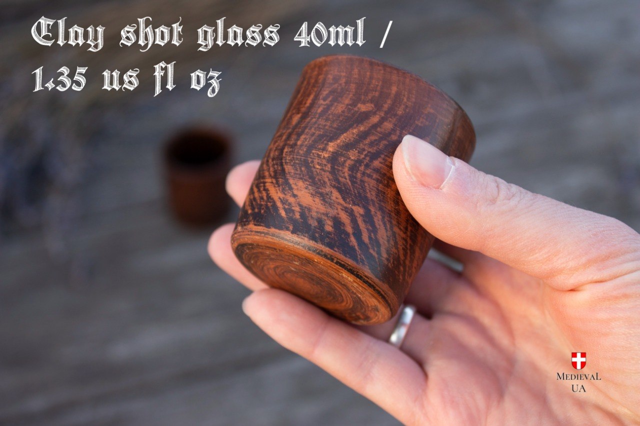 Handmade clay shot glass held between two fingers, 40 ml capacity