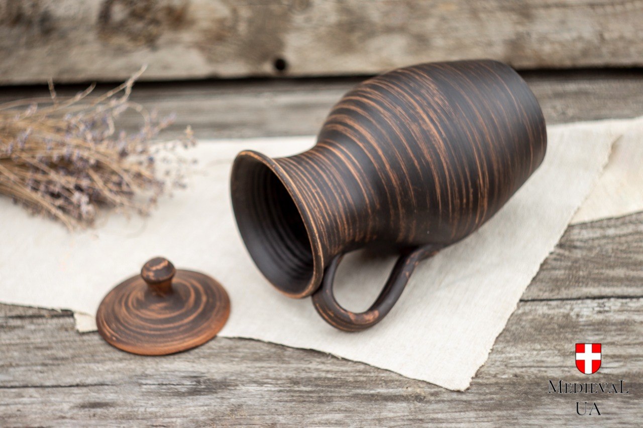 Handmade red clay jug lying on its side with lid removed, showing striped milk-fired surface
