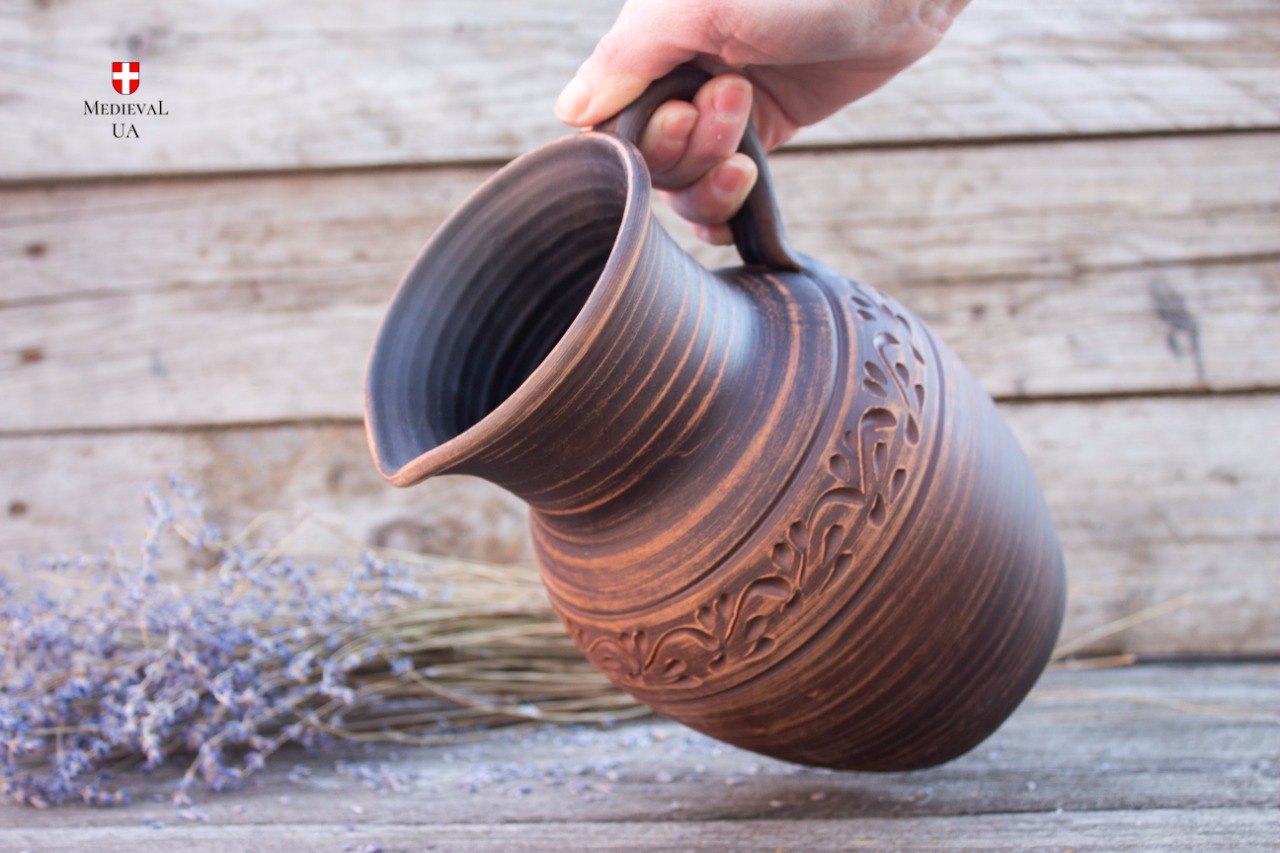 Large medieval pitcher held in hand, tilted to show pouring spout