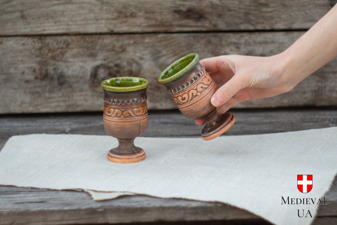 Pair of matching handmade pottery goblets with green-glazed interiors on a rustic wooden table