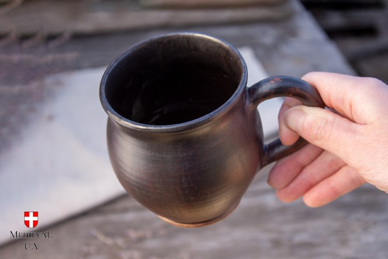 Hand holding the dark medieval tea mug, showing the black glazed interior and footed base