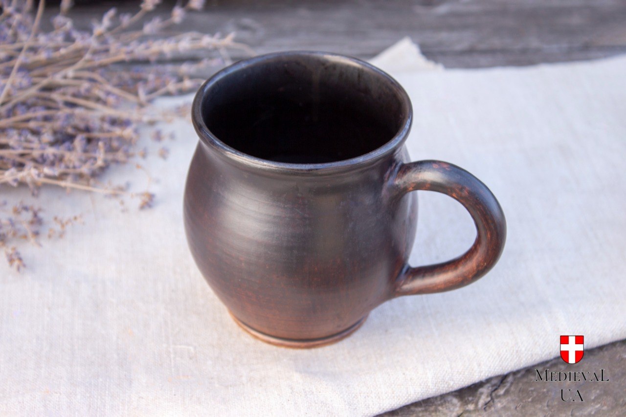 Round dark milk-fired medieval tea mug on linen and weathered wood with dried lavender