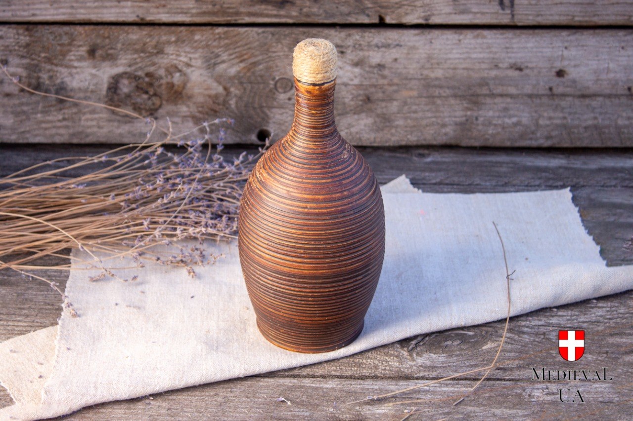Handmade clay bottle with a natural cork stopper standing on linen beside dried lavender