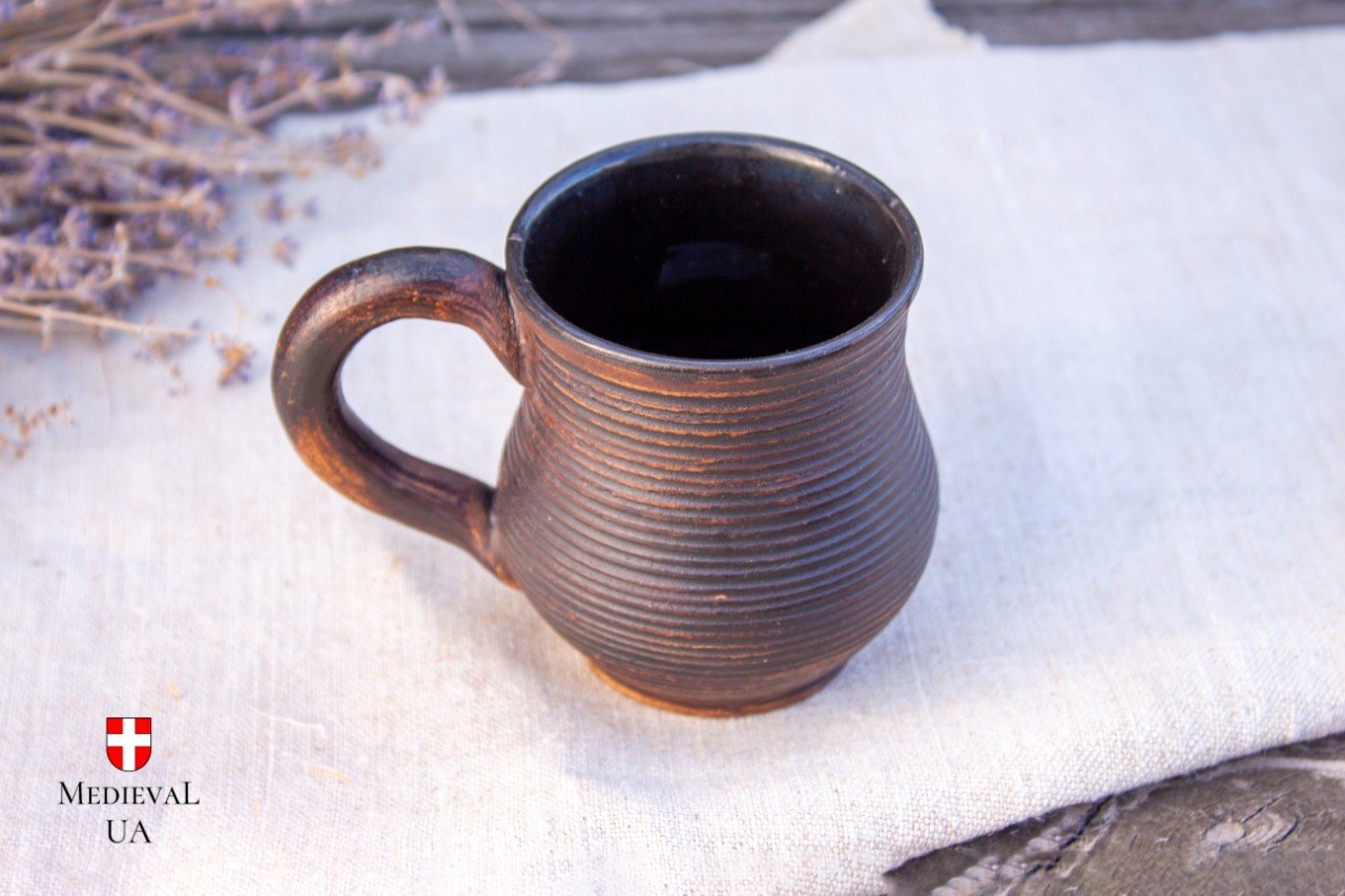 Ribbed dark brown milk-fired coffee cup on linen with dried lavender behind