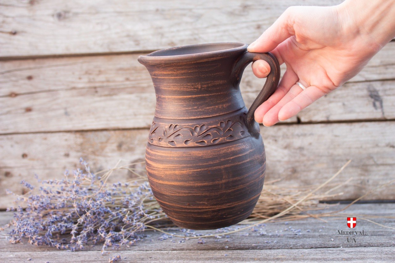 Handmade medieval clay jug held in hand beside dried lavender