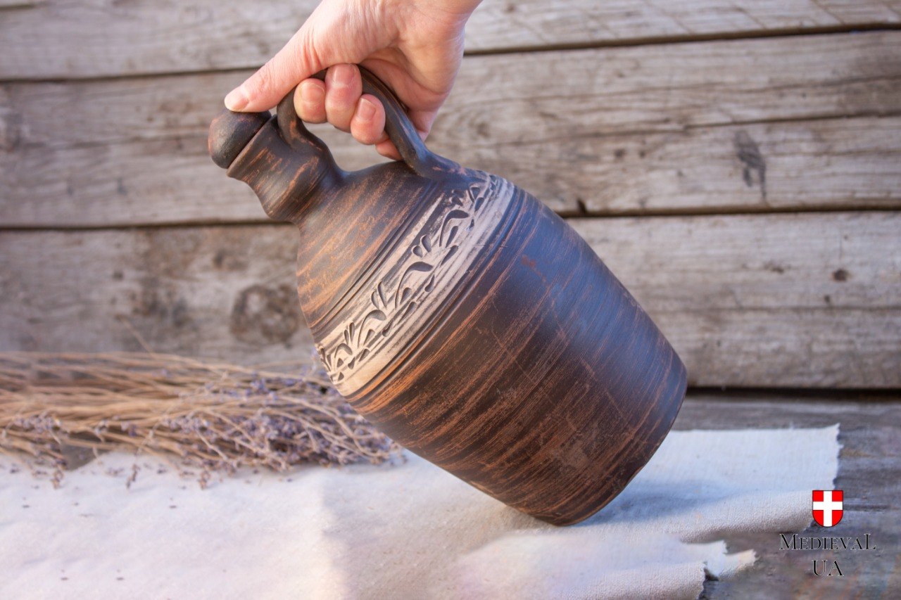 Hand lifting a milk-fired clay flagon by its pulled strap handle