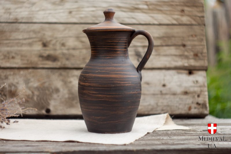 Milk fired red clay pitcher with a fitted lid standing on linen against weathered boards
