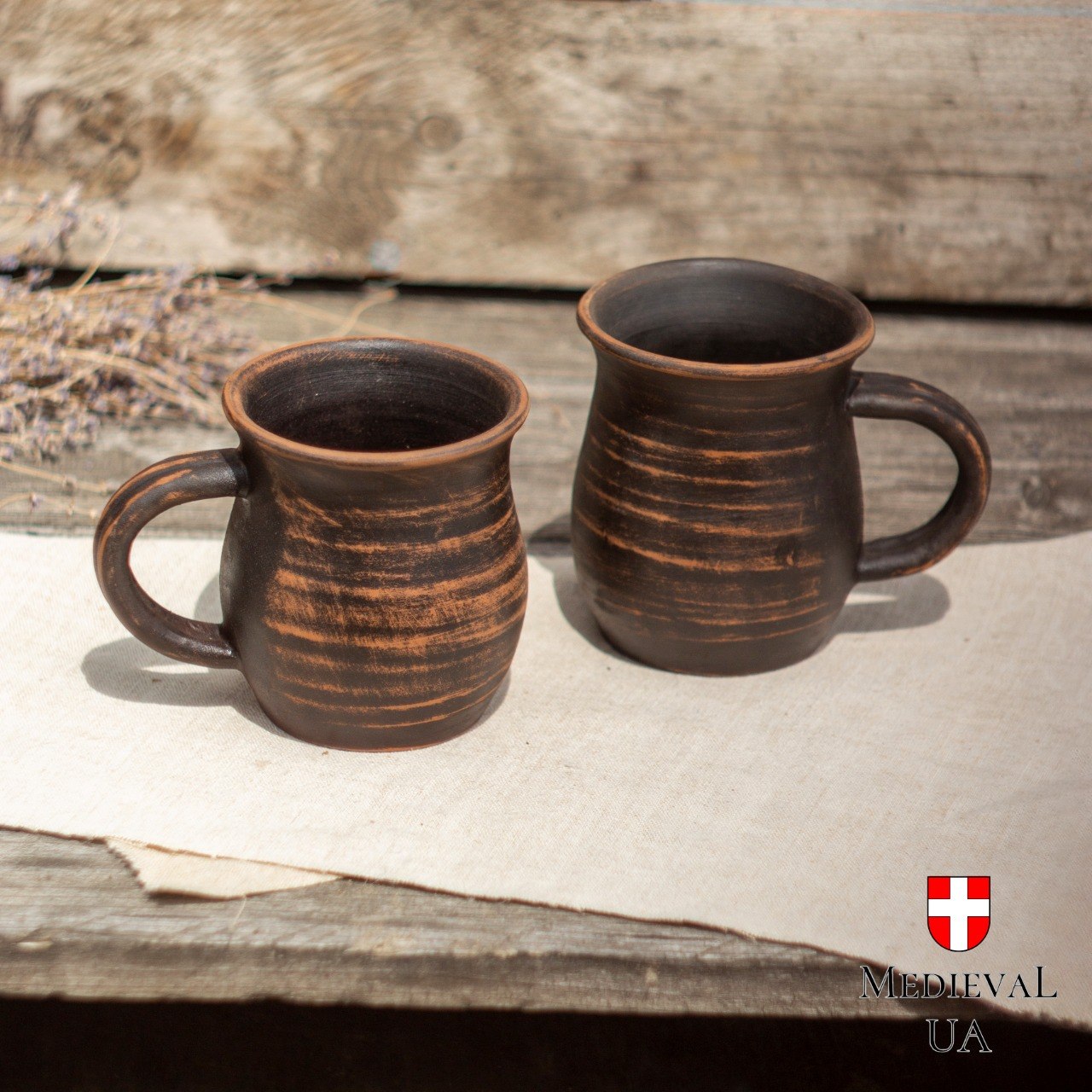 Pair of handmade milk-fired red clay feast mugs side by side on linen in daylight