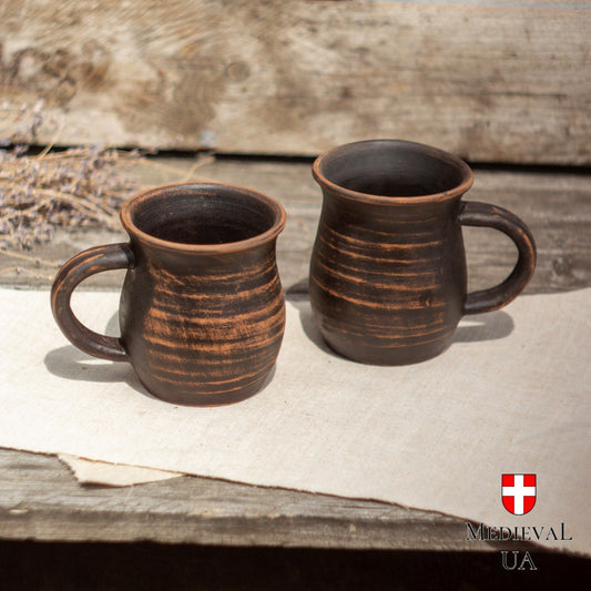 Pair of handmade milk-fired red clay feast mugs side by side on linen in daylight