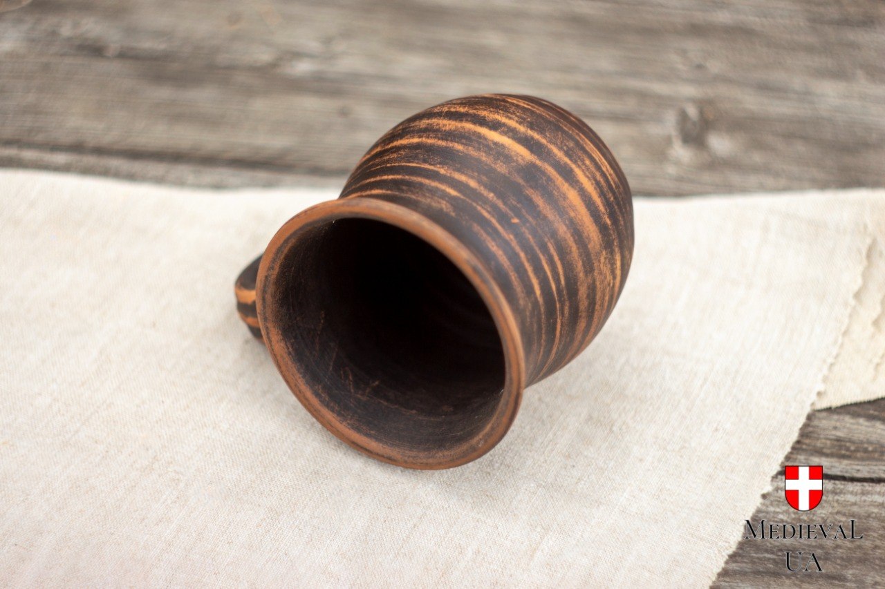 Handmade milk-fired red clay mug lying on linen, showing streaked brown surface and rounded body