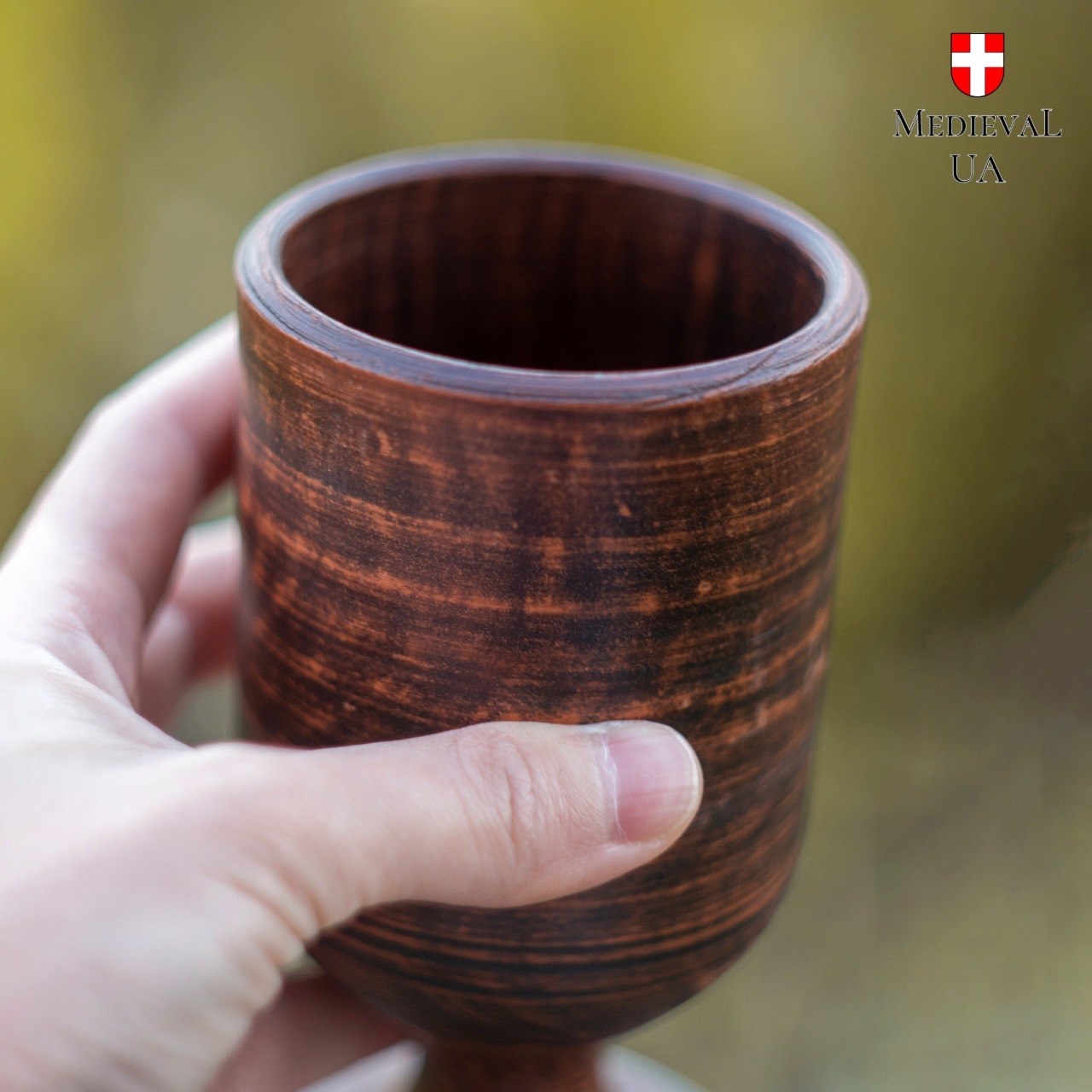 Close-up of a red clay goblet held in hand, showing streaked wood-grain milk-fired texture