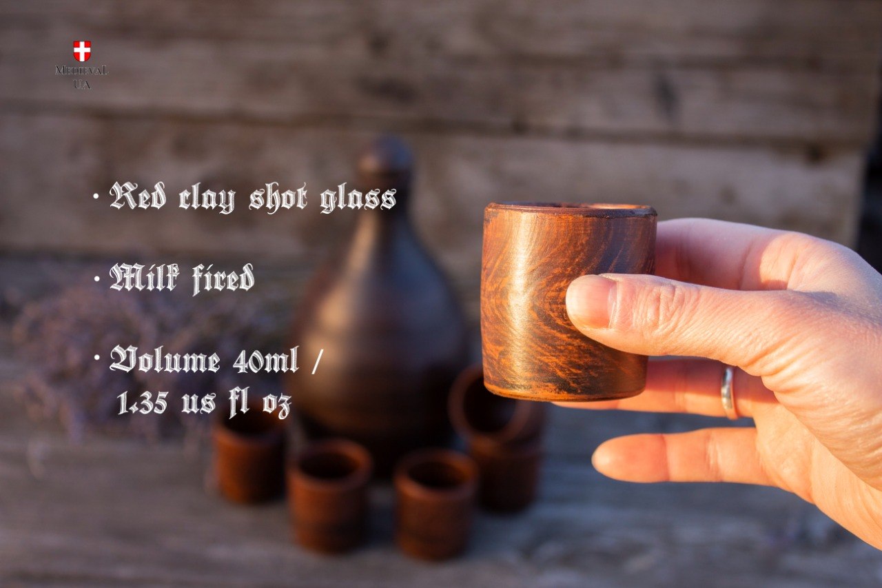 Red clay 40 ml shot cup in hand with a mead bottle behind