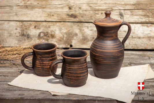 Complete three-piece red clay set with lidded jug and two mugs on rustic wood