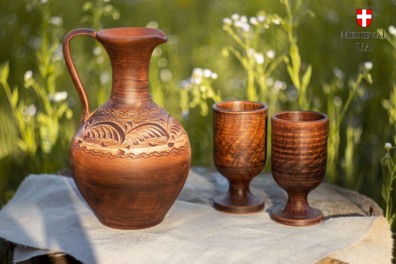 Complete red clay wine set with carved pitcher and two goblets in a summer meadow