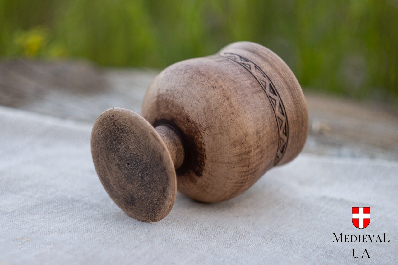 Underside of a rustic pottery goblet showing its turned stem and footed base on natural linen