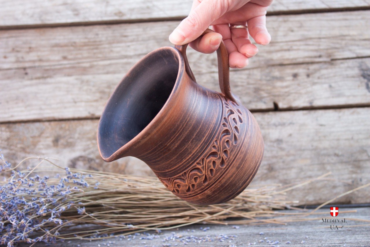 Small medieval clay pitcher held in hand, tilted to show spout
