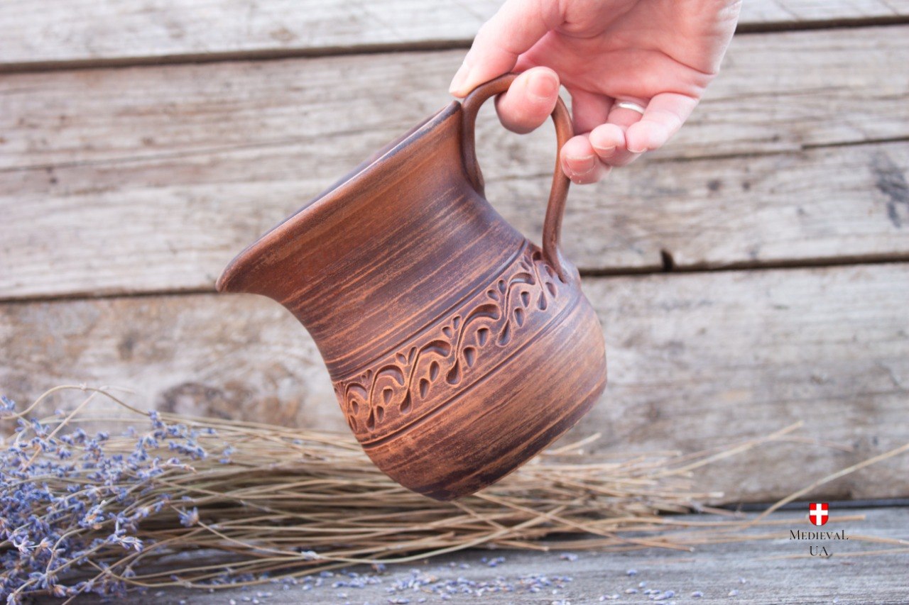Small medieval pitcher held by handle showing carved ornament