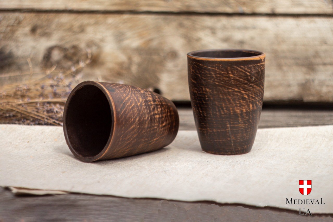 Two handmade unglazed clay cups, one tipped to show the smooth dark interior