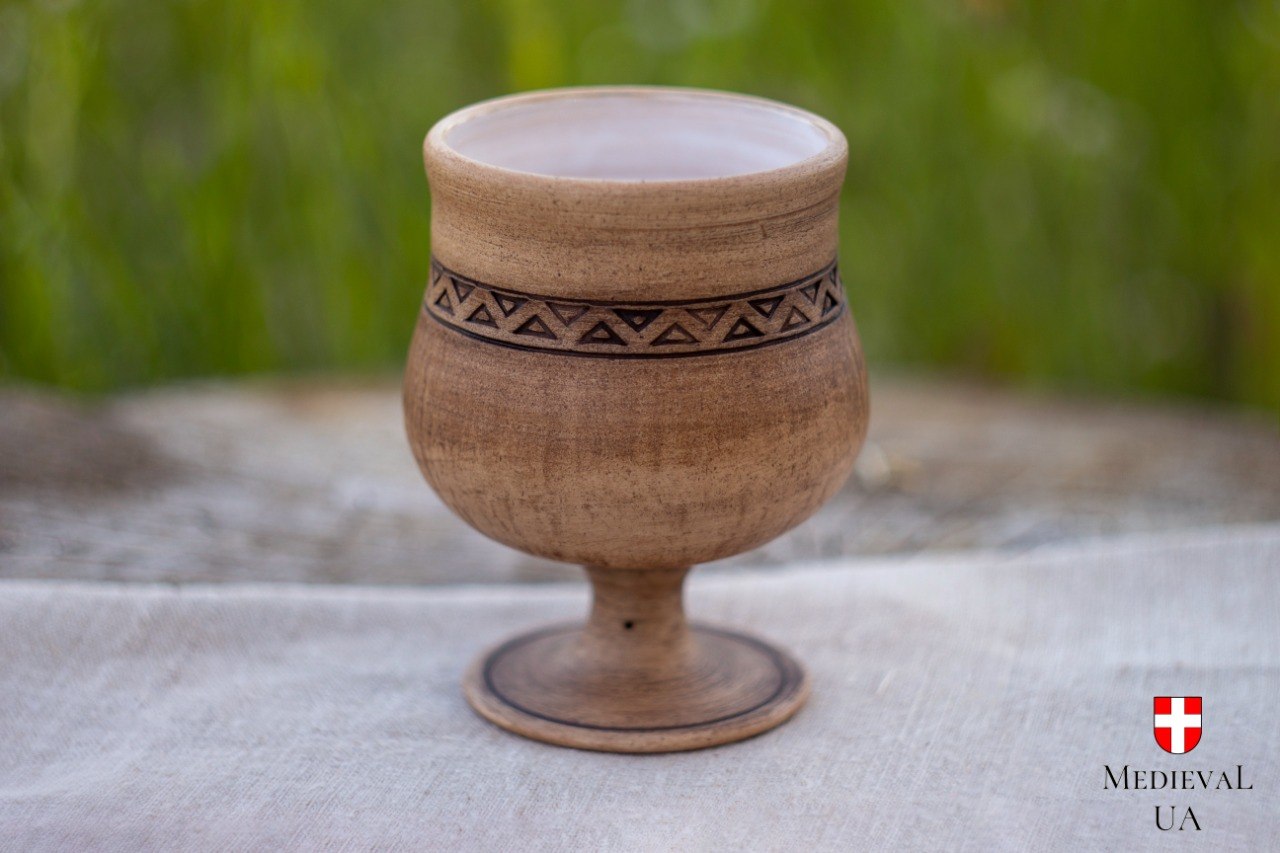 Front view of a wheel-thrown ceramic goblet with folk geometric carving and a white-glazed interior