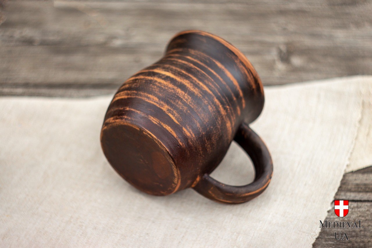 Rustic wheel-thrown clay mug resting on its side, revealing sturdy looped handle and milk-fired finish