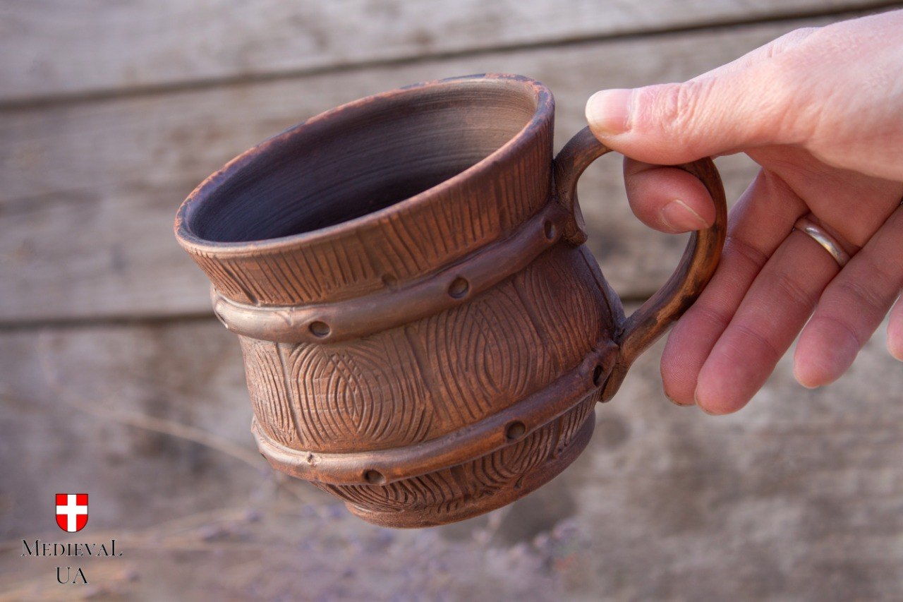 Barrel-shaped milk-fired clay mug on linen and weathered wood, three-quarter view