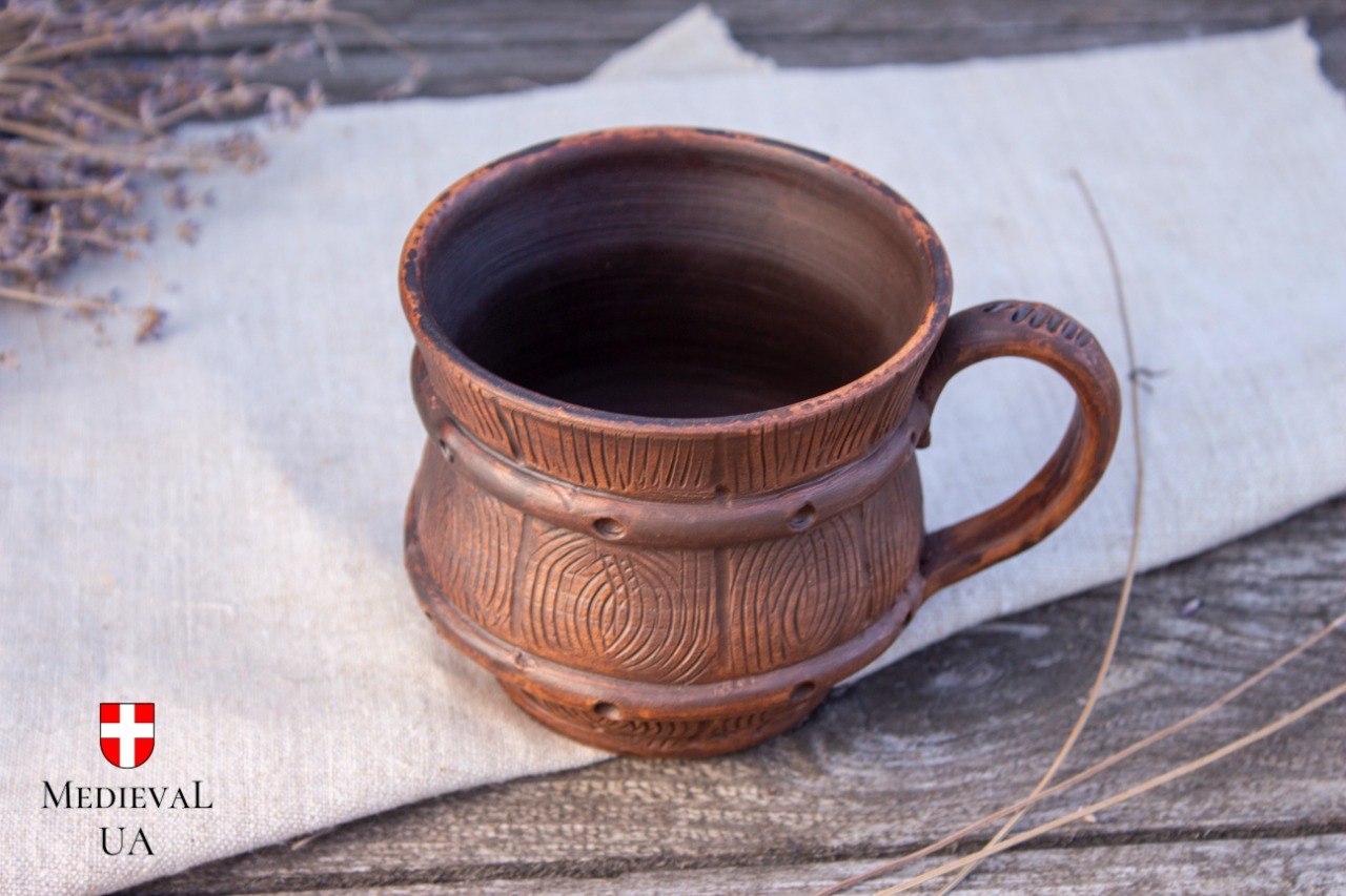 Barrel-shaped milk-fired clay mug on linen and weathered wood, three-quarter view